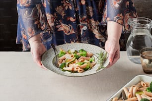 a woman is holding a bowl of pasta and broccoli