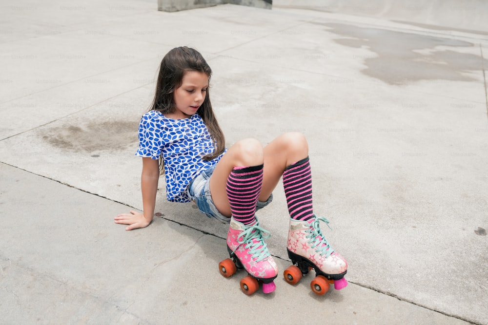 a little girl sitting on a skateboard with her feet on the ground