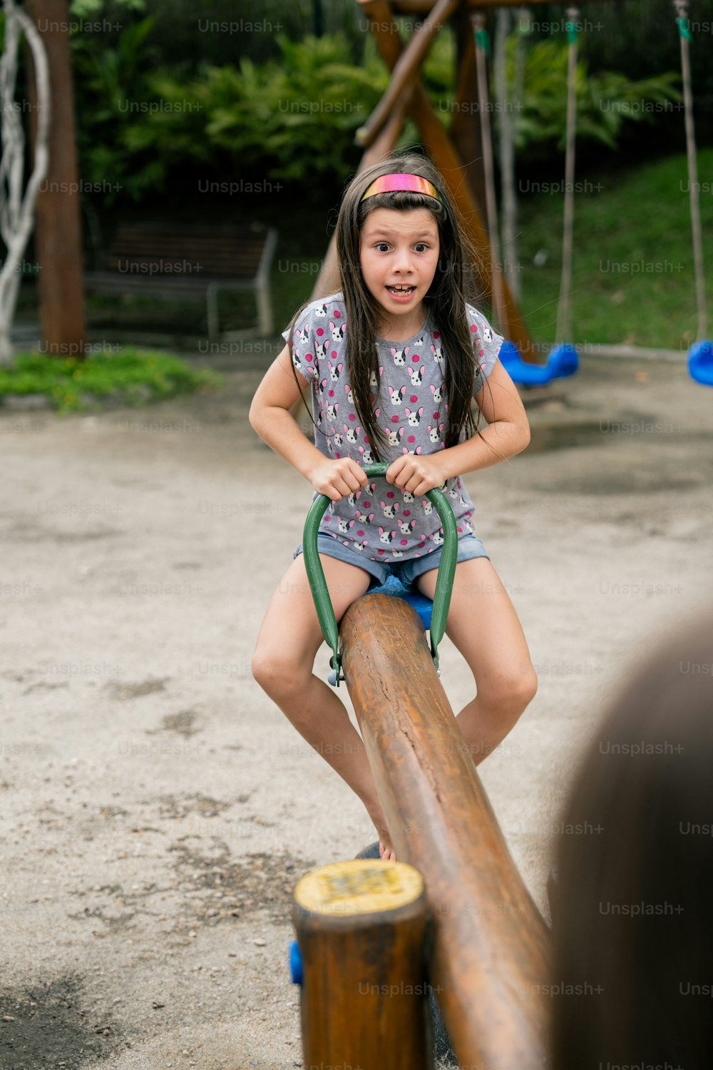 a little girl riding a wooden log on a playground