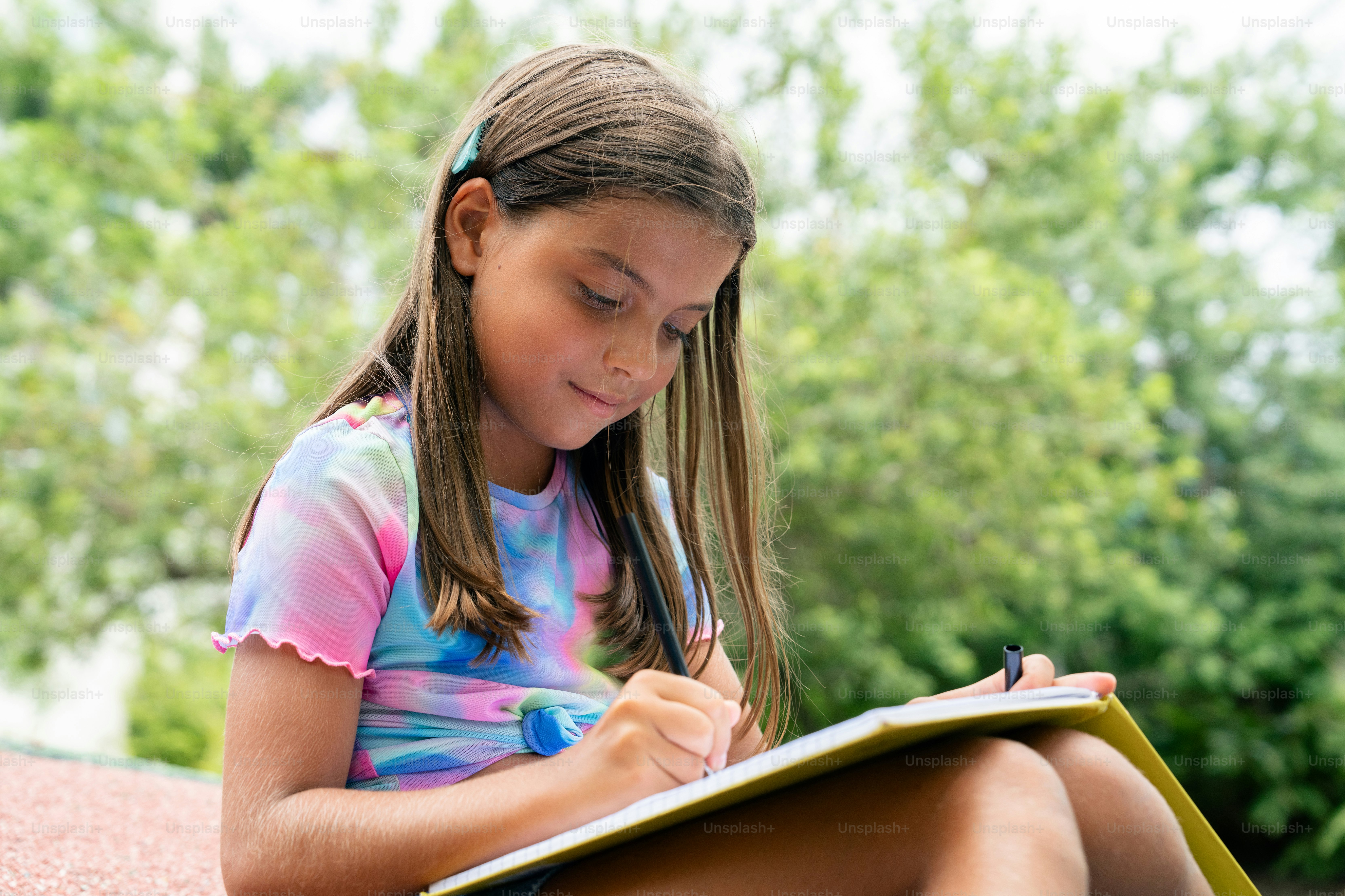 A little girl sitting on the ground writing on a piece of paper photo ...