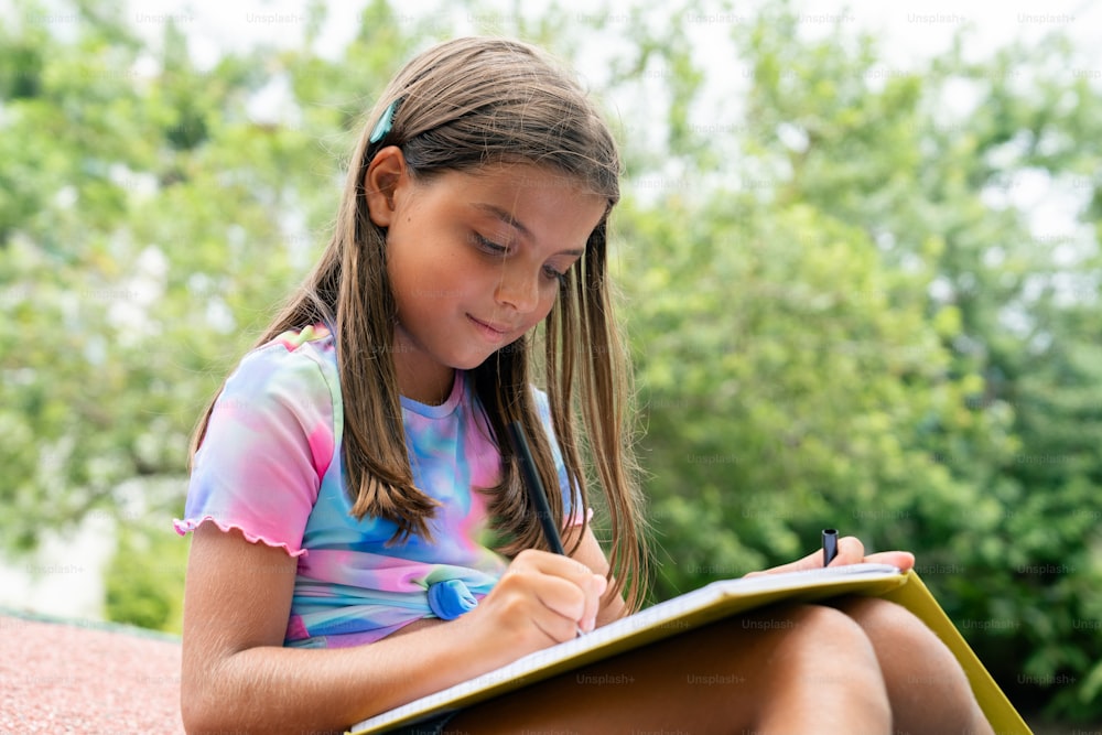 a young girl sitting on the ground writing in a notebook