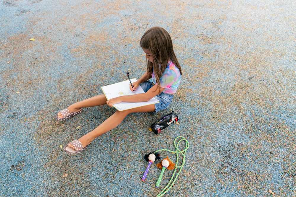 une petite fille assise sur le sol en train d’écrire sur un morceau de papier