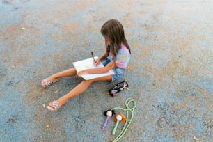 une petite fille assise sur le sol en train d’écrire sur un morceau de papier
