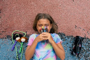 a little girl sitting on the ground with a bunch of crayons