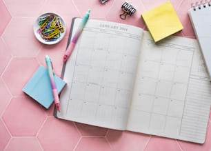 a calendar, pens, markers, and other office supplies on a pink surface