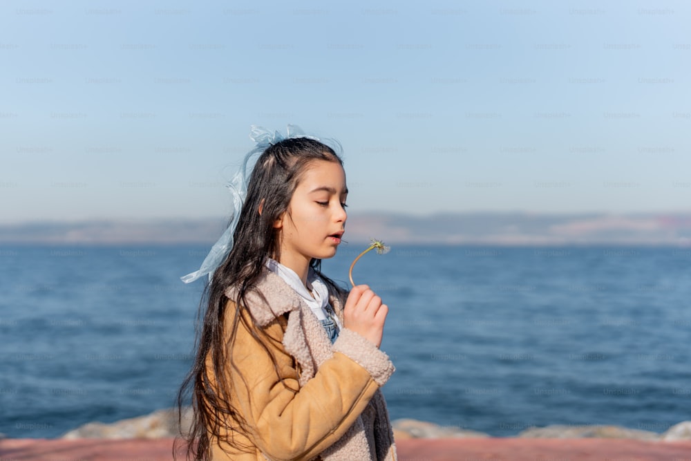 a little girl standing by the ocean blowing a dandelion