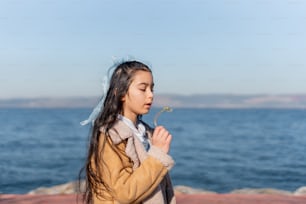 a little girl standing by the ocean blowing a dandelion