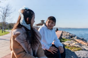 a woman sitting next to a boy on a rock near the ocean