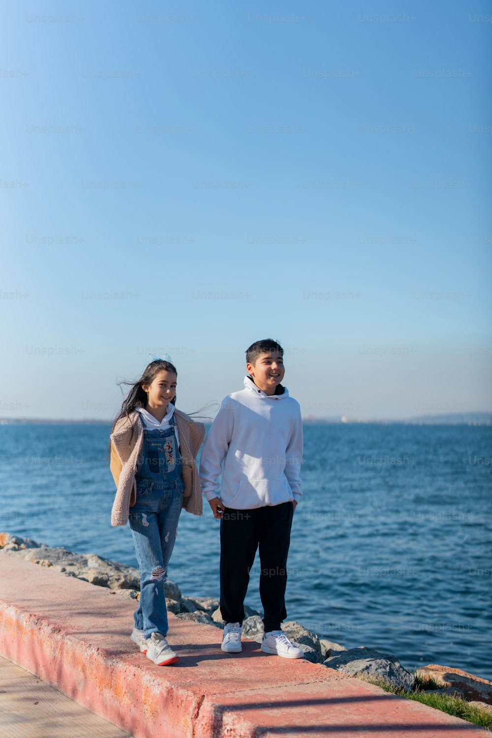 a man and a woman standing on a brick wall next to the ocean