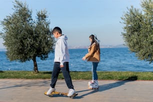 a boy and a girl are skateboarding by the water