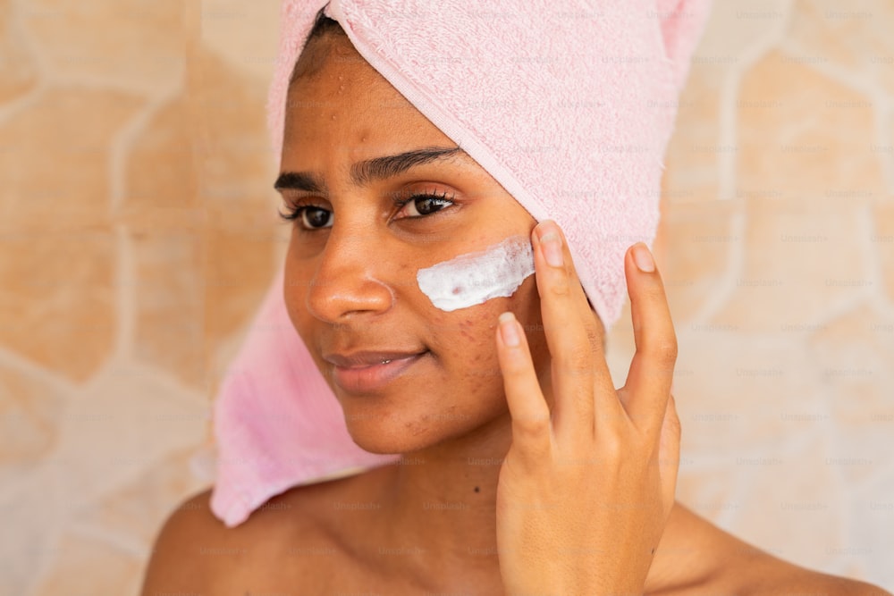 a woman with a towel on her head is putting a cream on her face