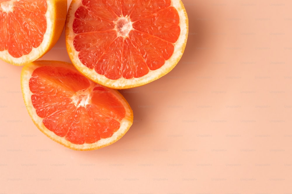 three grapefruits cut in half on a pink background