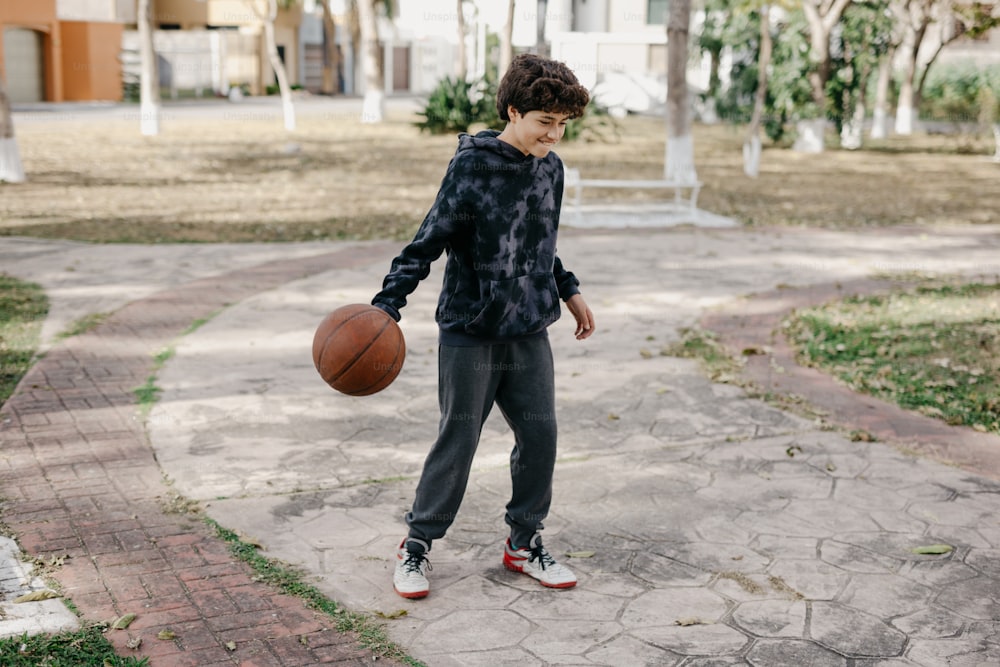 a young man holding a basketball on a sidewalk