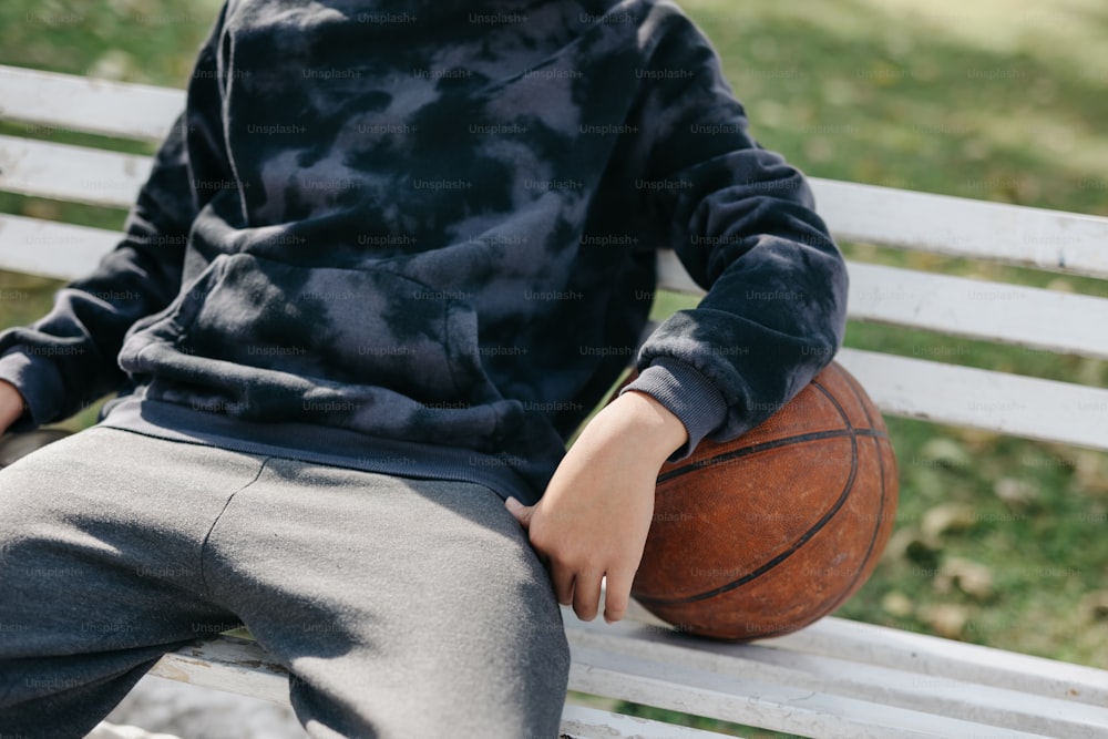 a young boy sitting on a bench holding a basketball