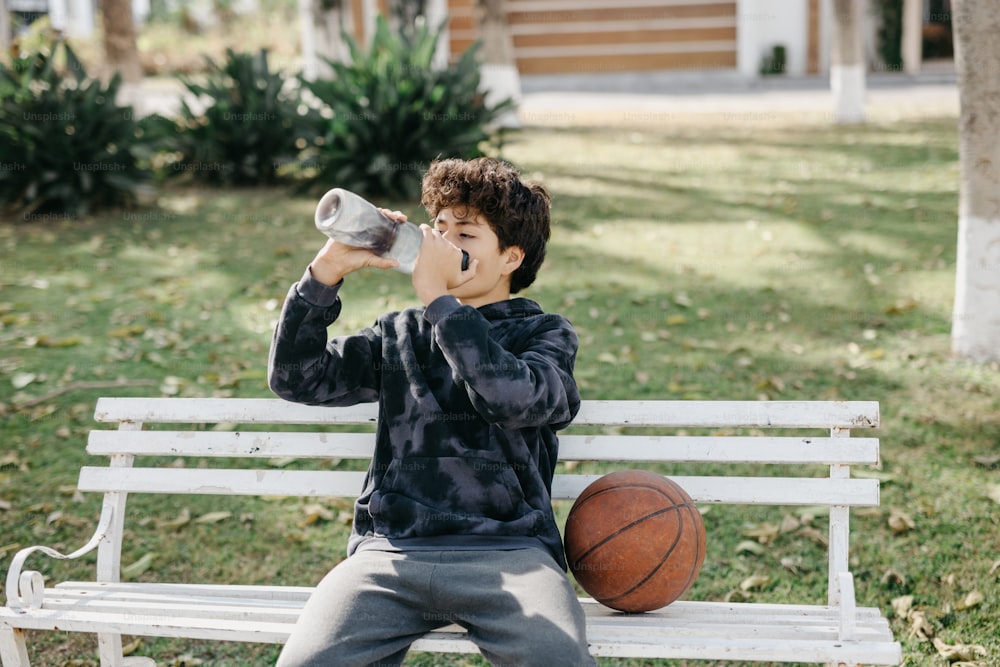 Ein kleiner Junge sitzt auf einer Bank und trinkt aus einer Flasche