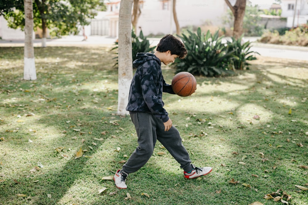 a young boy holding a basketball in a park