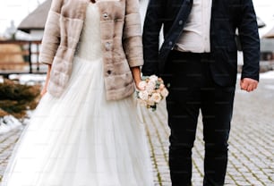 Eine Braut und ein Bräutigam, die Händchen haltend eine Kopfsteinpflasterstraße entlang gehen