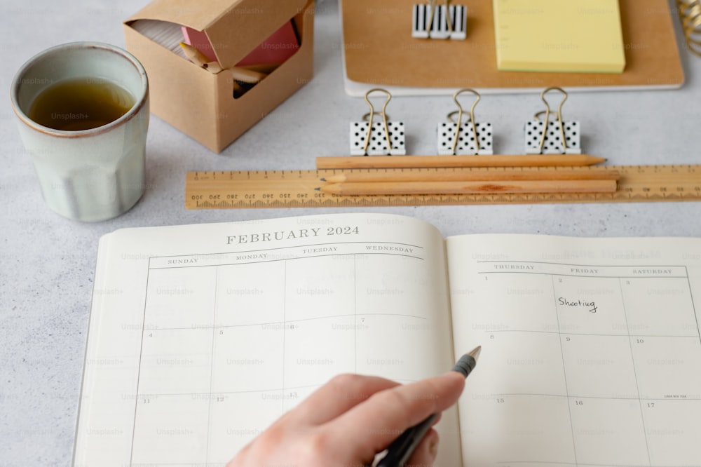 a person holding a pen and writing on a calendar