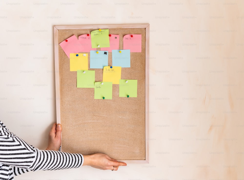 a woman holding a bulletin board with post it notes on it