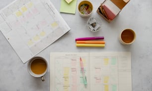 a desk with a planner, cup of coffee and a pen