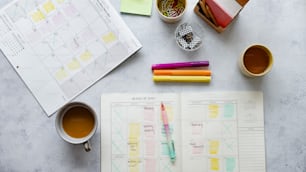 a desk with a planner, pens, and a cup of coffee