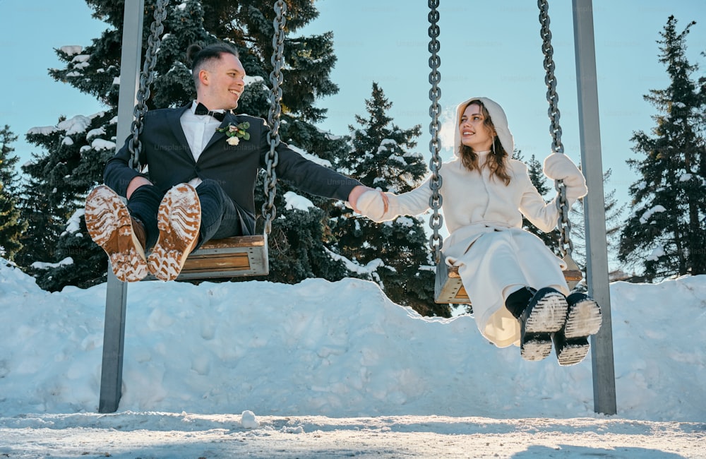 a bride and groom sitting on a swing in the snow