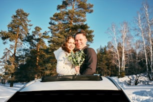 a man and woman standing on top of a car in the snow