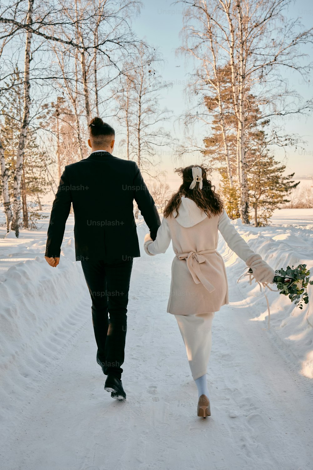 Ein Mann und eine Frau, die Händchen haltend im Schnee spazieren gehen