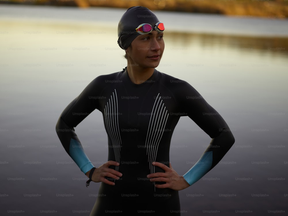 a woman in a wet suit and goggles standing next to a body of water