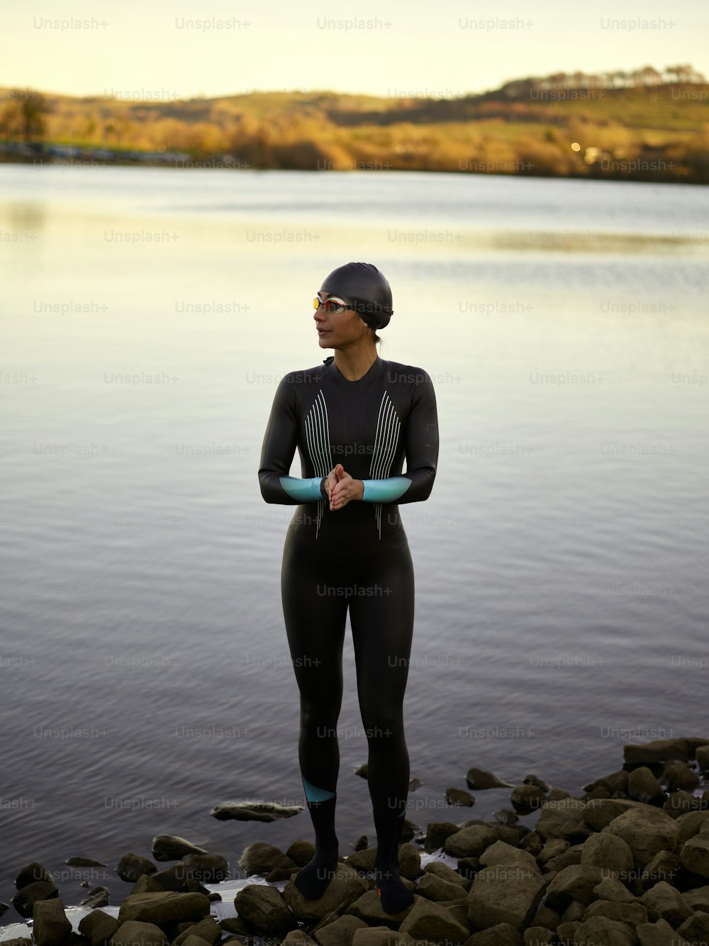 a woman in a wet suit standing on rocks near a body of water