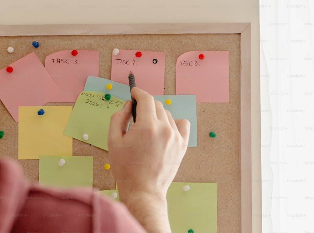 a person writing on a bulletin board with sticky notes