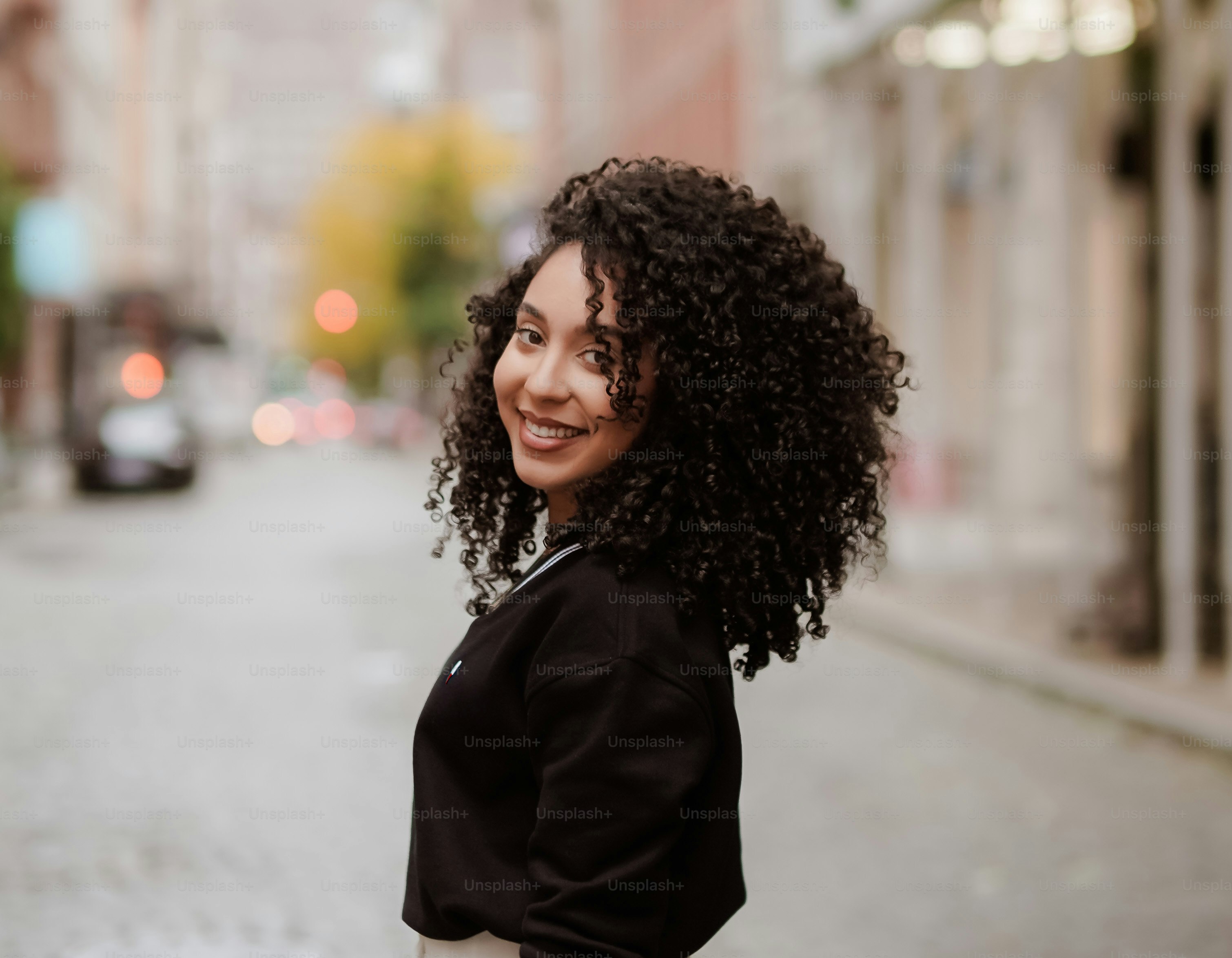 une femme aux cheveux bouclés debout dans une rue de la ville