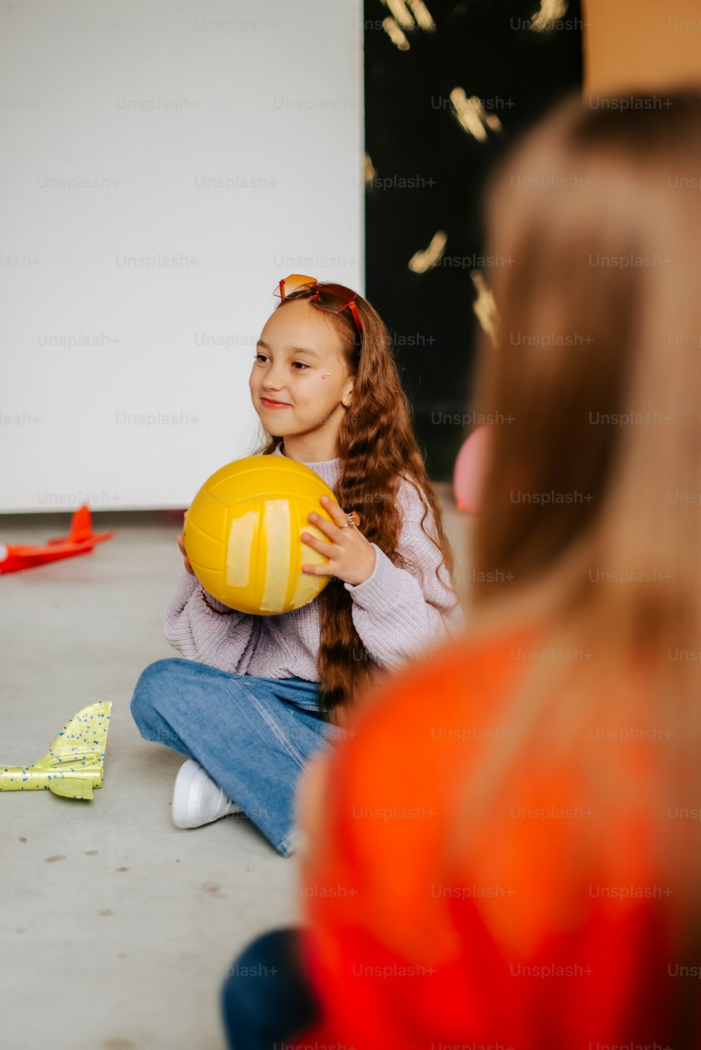 a little girl sitting on the floor holding a yellow ball