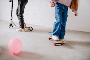 a couple of kids riding scooters next to a pink ball