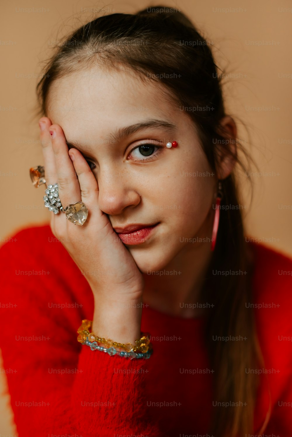 a young girl wearing a red sweater holding her hand to her face