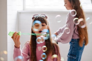 a little girl blowing bubbles while another girl watches