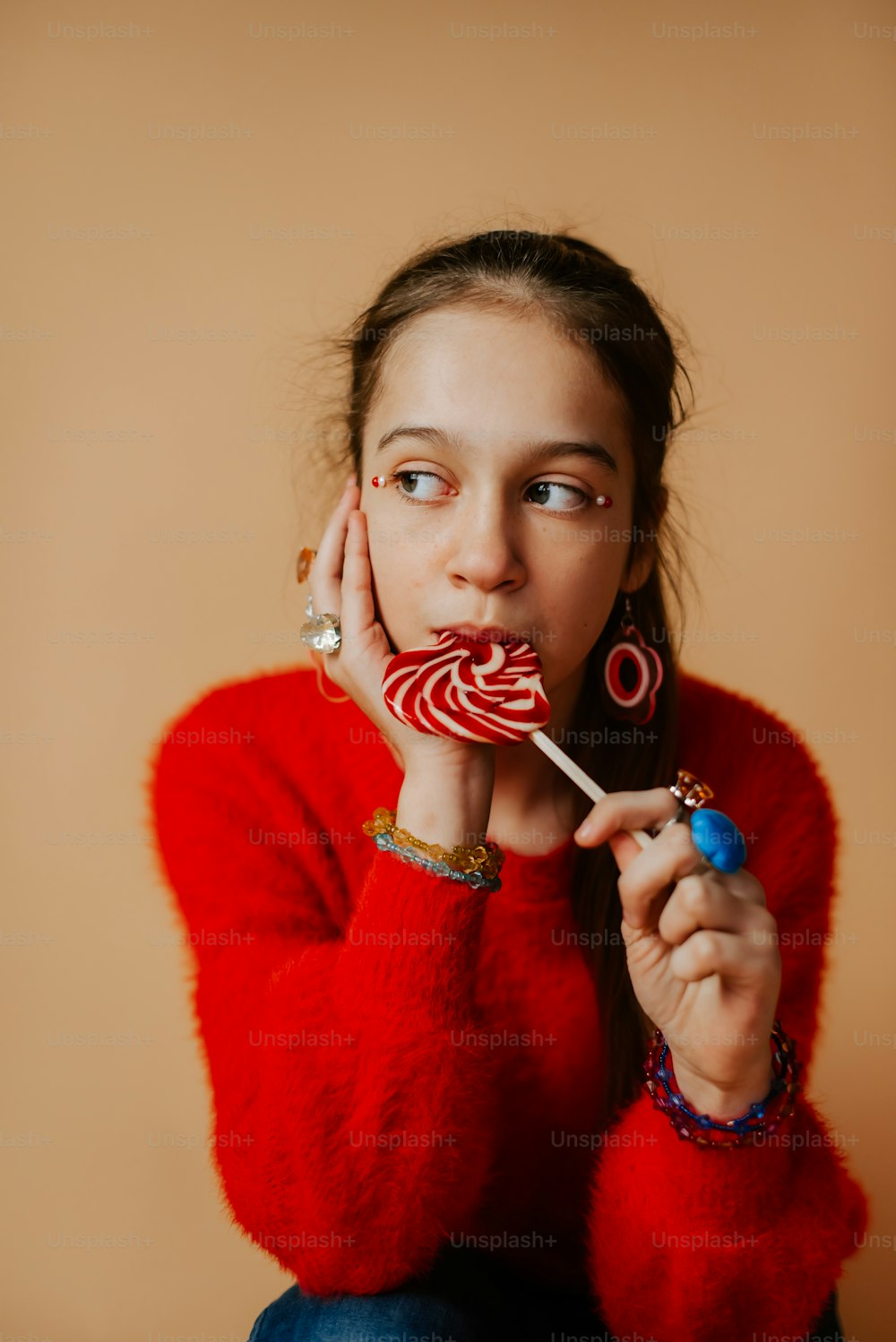 a girl in a red sweater holding a lollipop