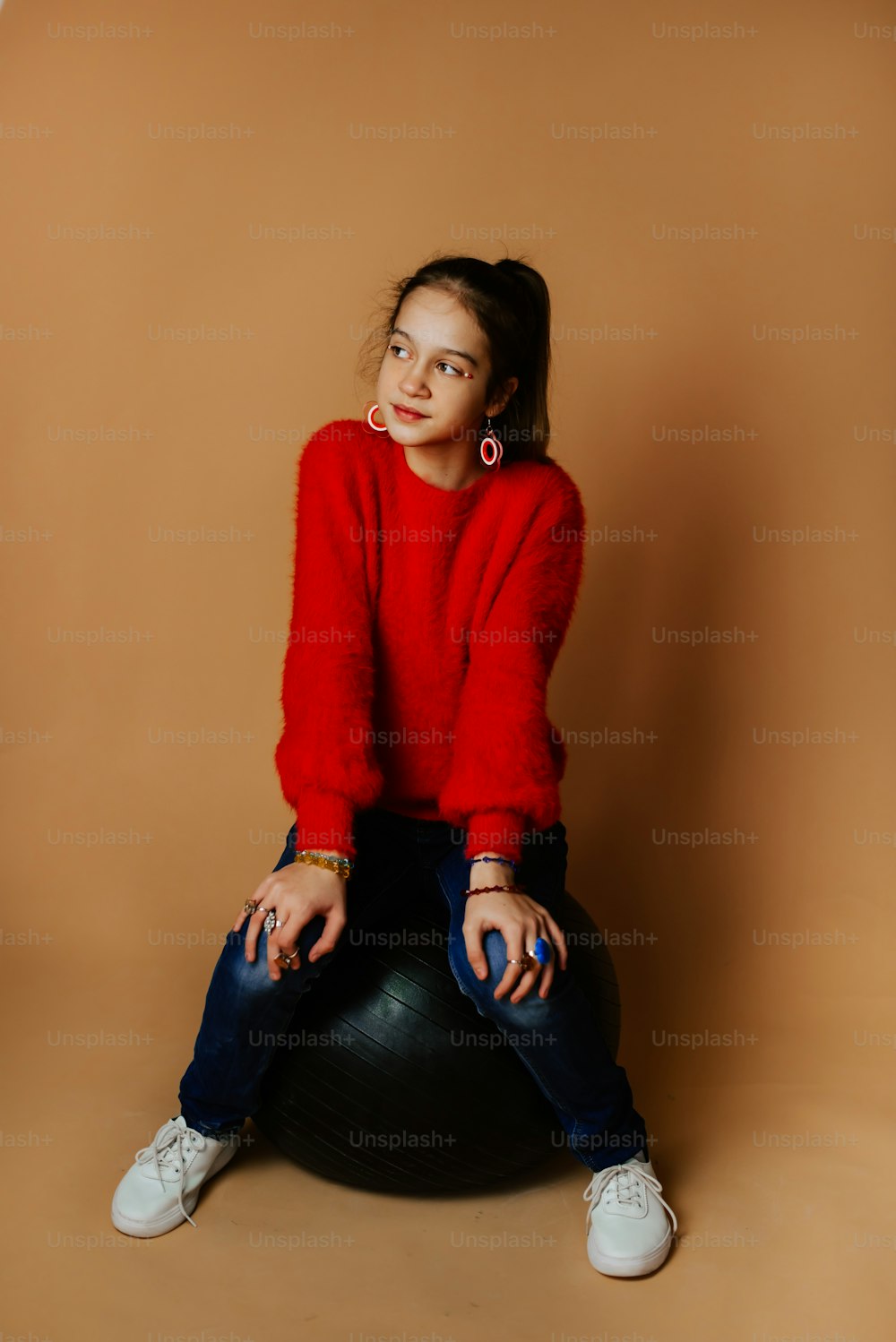 a woman in a red sweater is sitting on a black ball