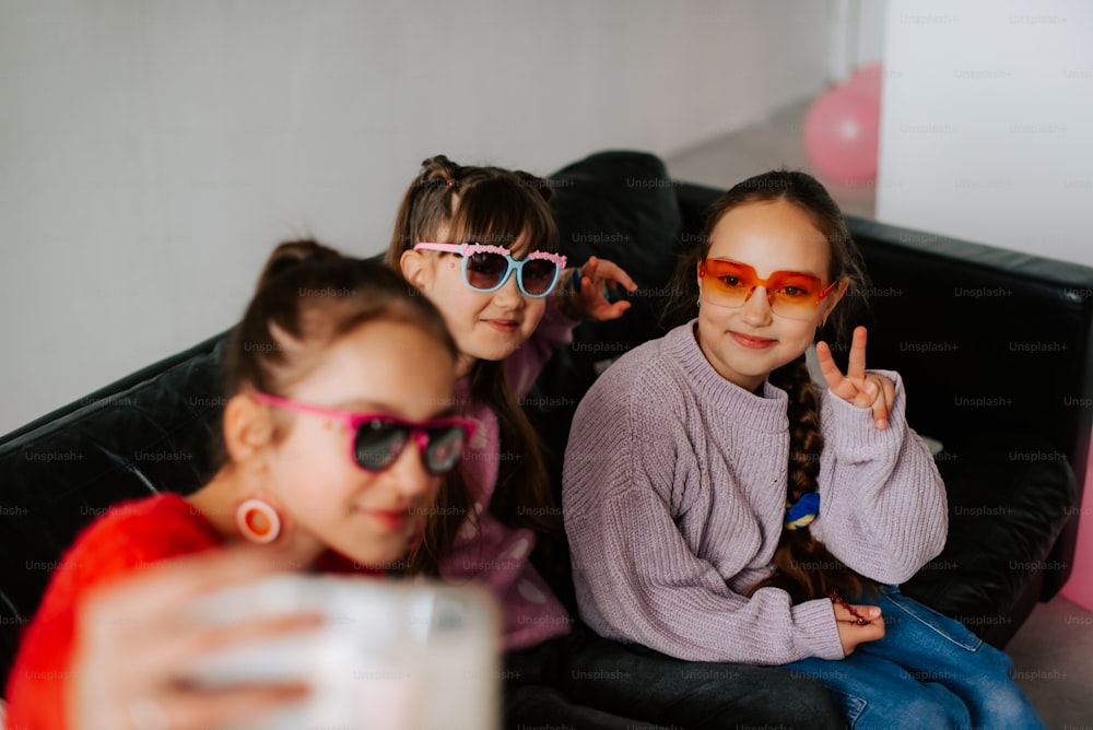 three little girls sitting on a couch wearing sunglasses