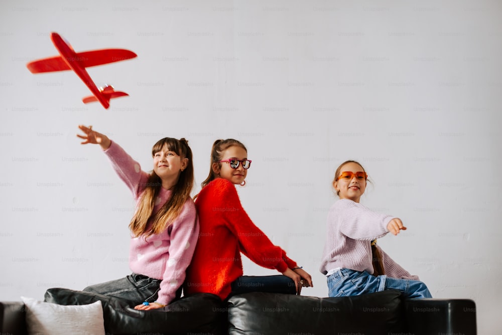 three girls sitting on a couch with a toy plane in the air