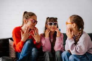 three little girls sitting on a couch wearing sunglasses