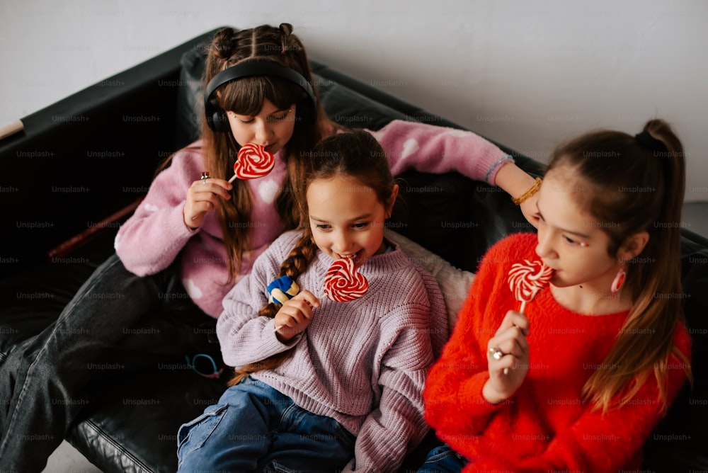 three girls sitting on a couch eating lollipops