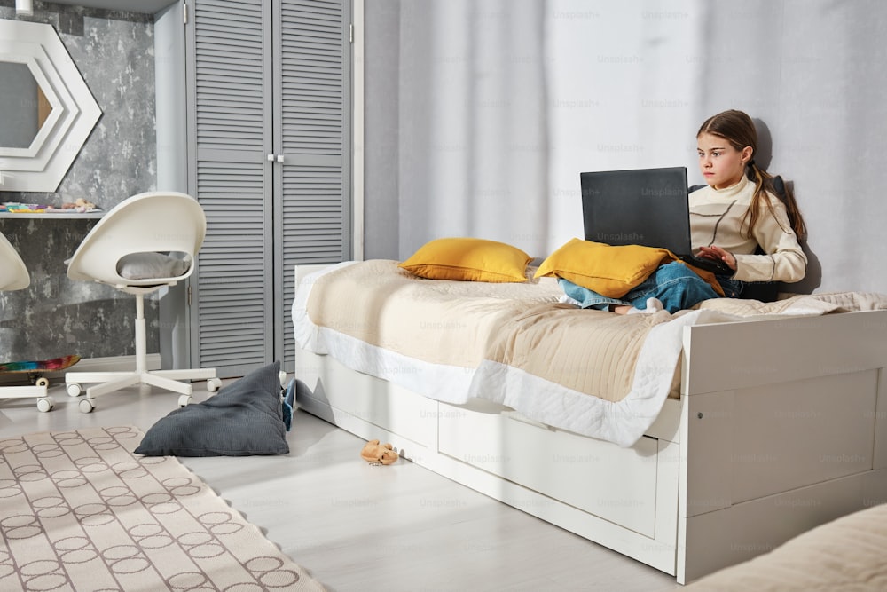 une fille assise sur un lit avec un ordinateur portable