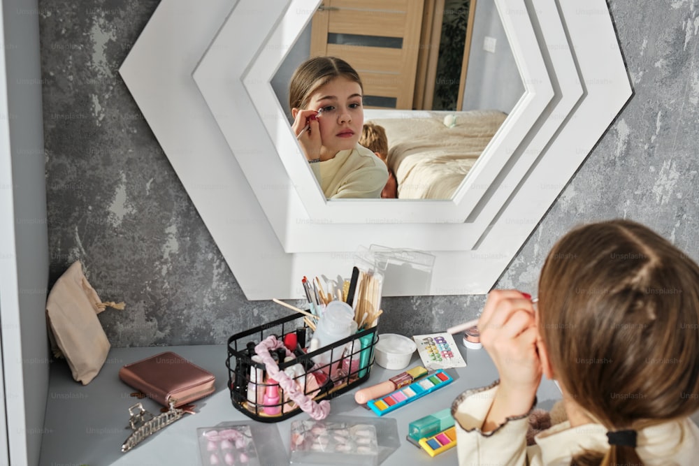 거울에 비친 자신의 화장을 보고 있는 어린 소녀
