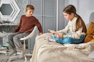 a boy and a girl sitting on a bed looking at a cell phone