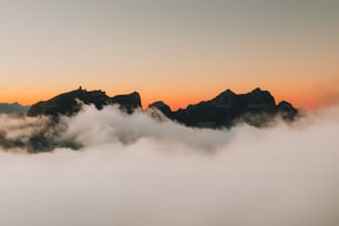 un gruppo di montagne tra le nuvole con un tramonto sullo sfondo