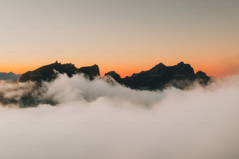 un grupo de montañas en las nubes con una puesta de sol en el fondo