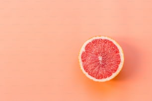 a grapefruit cut in half on a pink background