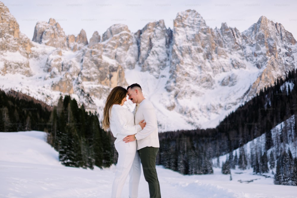 a man and woman standing in the snow with mountains in the background