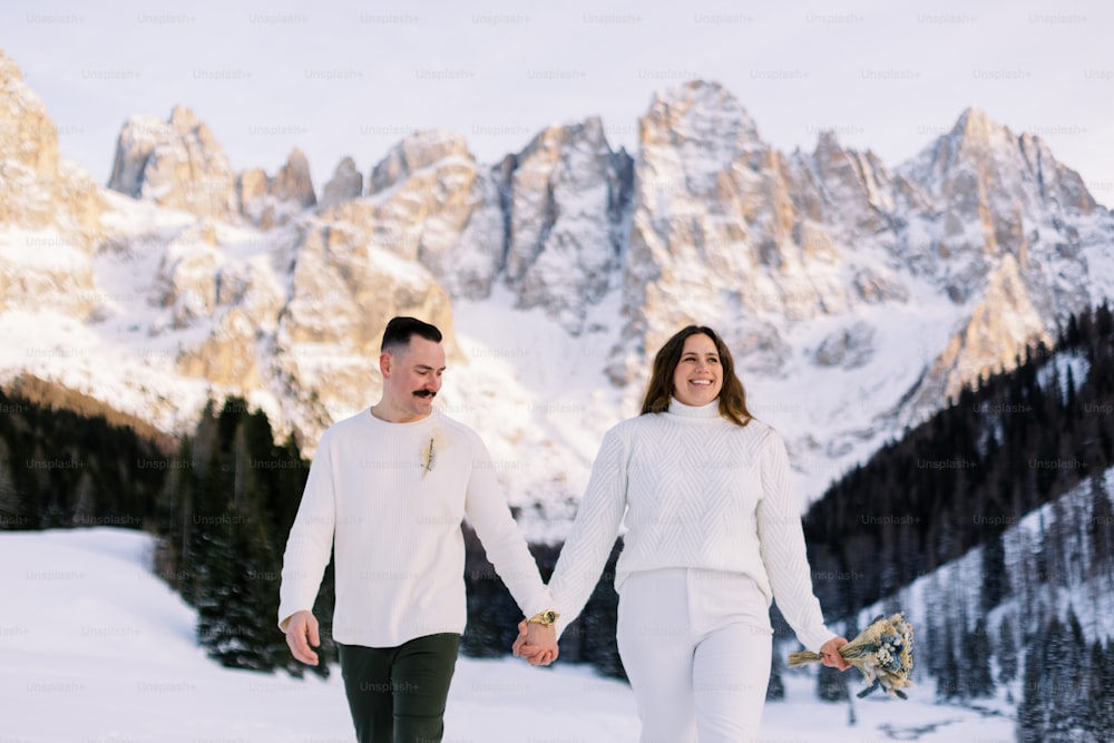 a man and woman holding hands while walking in the snow